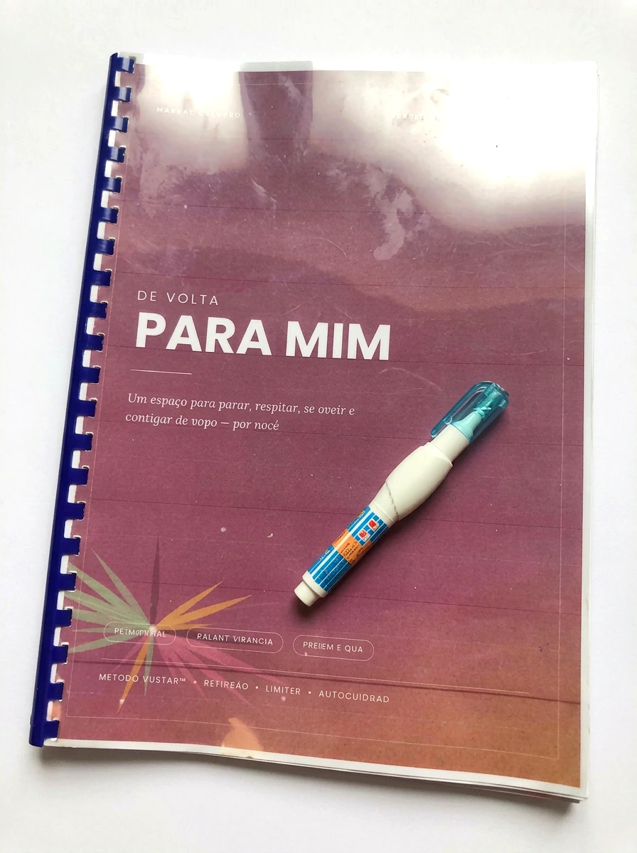 Foto real do material De Volta Para Mim impresso, encadernado, ao lado de uma caneta